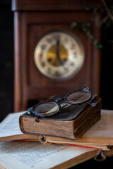 Old holy Bible, books and glasses on wooden table with vintage clock in background