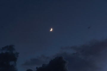 A scenic shot of the crescent moon shining in the cloudy night sky
