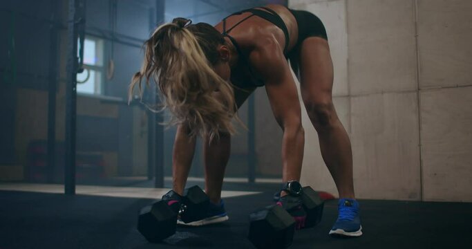 A woman performs push-UPS with dumbbells. burpee with weight. The jerk of the dumbbells over your head. A woman trains with a heavy weight.