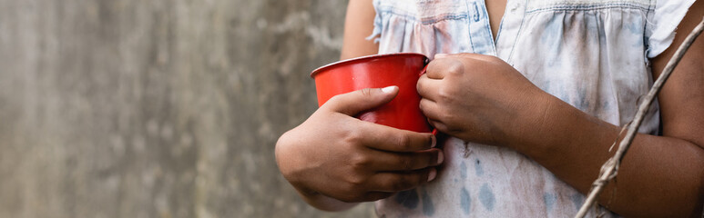 Panoramic crop of poor african american child holding metal cup on urban street