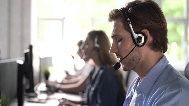 Focused male representative call center agent in wireless headset helping client with complaints using computer in office, corporate operator working in customer support service on helpline telesales