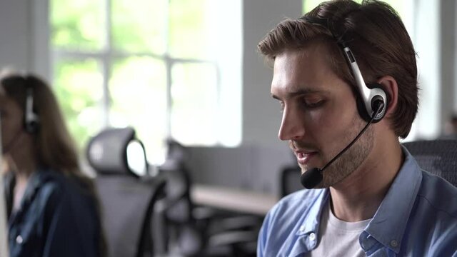 Focused male representative call center agent in wireless headset helping client with complaints using computer in office, corporate operator working in customer support service on helpline telesales