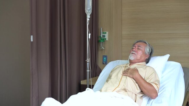 asian senior man patient coughing while lying on bed at hospital ward . Lonely old man looking away in Nursing home.
