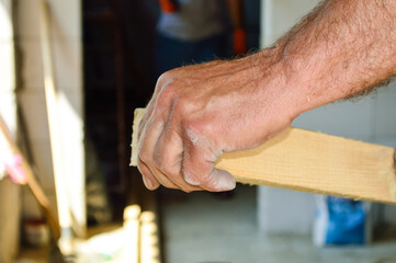 close-up - male hand holding the end of a wooden board, against the background of the construction site