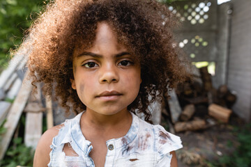 selective focus of poor african american child in torn clothes looking at camera outside