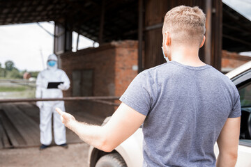 Checking and disinfecting car for virus COVID-19 and bubonic plague border of city and country. Doctor in biohazard suit informs driver of danger
