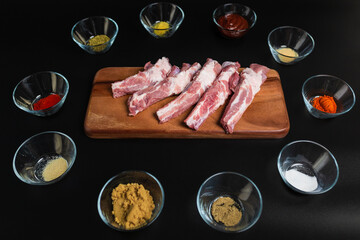 Close-up Raw Pork Ribs on a wooden board with lots of marinating spices around on a black background with free space for your text/decoration.
