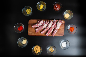 Close-up Raw Pork Ribs on a wooden board with lots of marinating spices around on a black background with free space for your text/decoration.