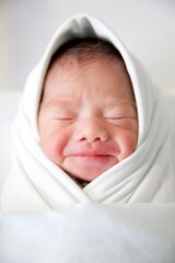 New born baby in a wrap on white blanket.