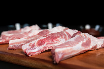 Close-up Raw Pork Ribs on a wooden board on a black background with free space for your text/decoration.