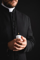 cropped view of bearded priest holding burning candle in hands isolated on black