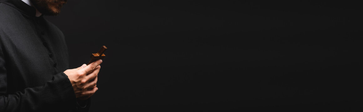 panoramic orientation of priest holding wooden cross isolated on black