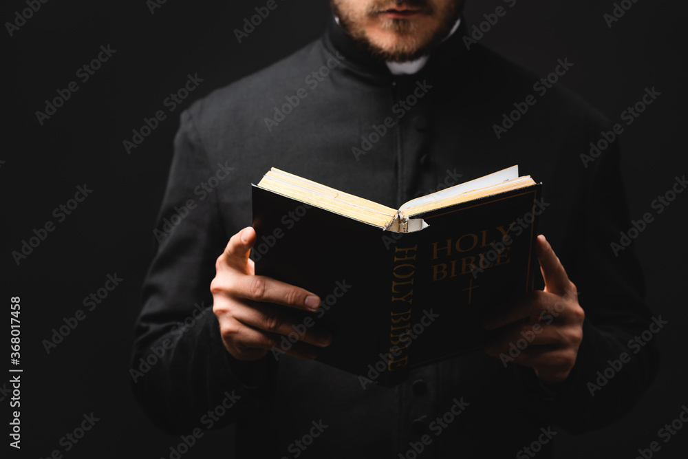 Wall mural partial view of bearded pastor reading holy bible isolated on black - Wall murals