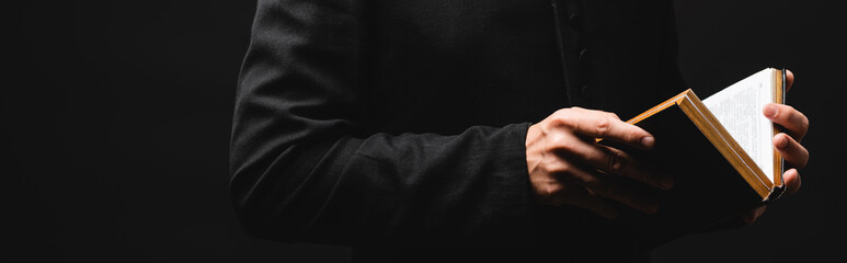 website header of priest holding holy bible in hands isolated on black - obrazy, fototapety, plakaty