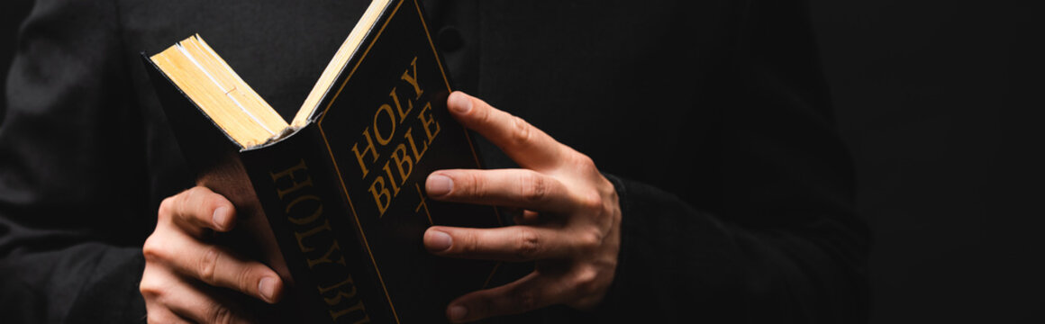 Horizontal image of pastor reading holy bible isolated on black