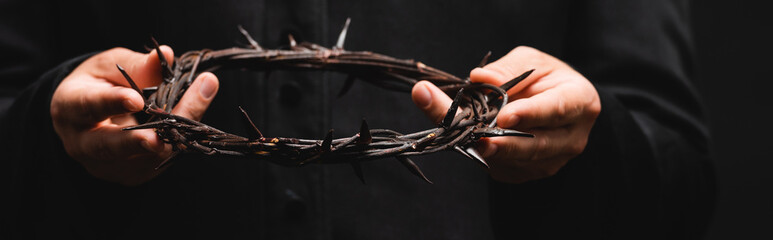 horizontal crop of priest holding wreath with spikes isolated on black