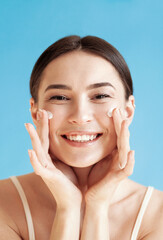 Lovely young woman with healthy skin is applying a cream on her face