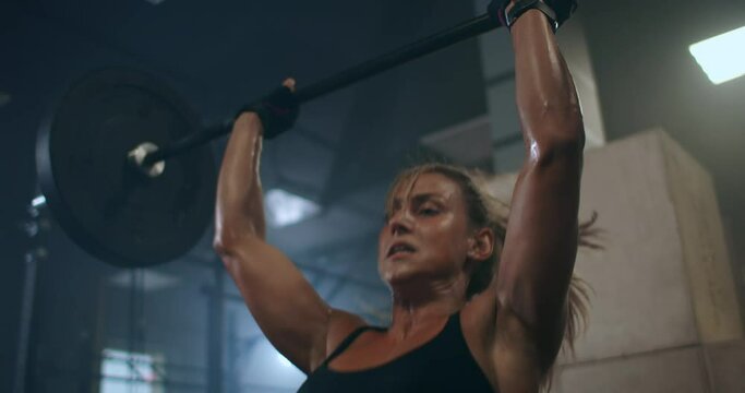 a female weightlifter performs a barbell lift in a dark gym. a woman lifting a heavy bar over her head