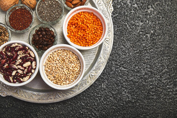 Beans and nuts selection in bowls: quinoa, chia, lentils, beans, almonds, walnuts, coffee beans on dark concrete background copy space