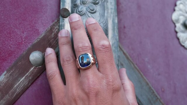 A hand with a ring touches the old texture of the grave door. Reflection is visible in the ring. Traditionally masculine jewelry of hands.