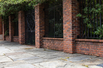 Tall brick and wrought iron wall beside a slate stone walkway, old architectural details, copy space, horizontal aspect