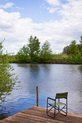 An empty chair and a fishing rod on a wooden pier by the lake. Outdoor recreation.