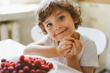 Cute beautiful little boy eating fresh raspberries. Healthy food, childhood and development. Happy kid at home.