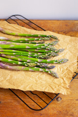 Fresh green asparagus spears wrapped in brown craft paper wrapper for healthy vegetarian cuisine lying on a wooden surface, top view. Close-up.