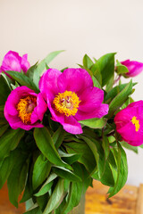 A bouquet of beautiful bright pink peonies in a glass vase stands on a wooden table. Close-up.