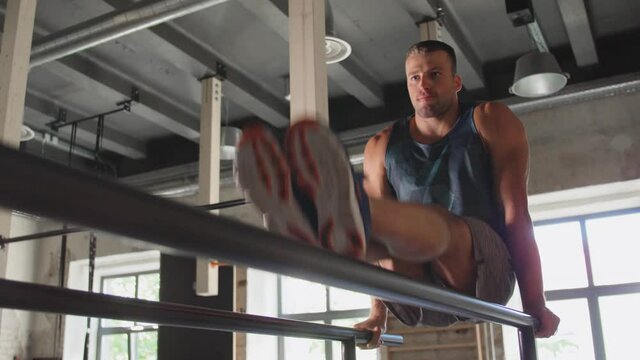 fitness, sport, bodybuilding and people concept - young man doing abdominal exercise on parallel bars in gym