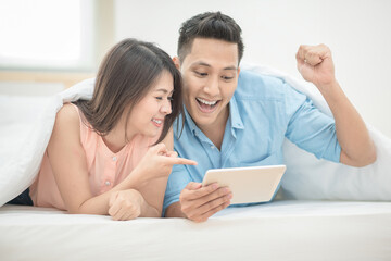 Obraz premium Asian couple lovers enjoy cheer up online esport on smart tablet on holiday vacation in bedroom.