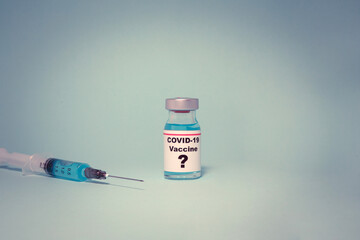 Small vaccine bottle (phial) with a label that reads "Covid - 19 Vaccine" and a question mark & a medical syringe isolated on blue background Vaccination for prevention, immunization and treatment