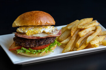 meat burger prepared with lettuce tomato ham cheese egg and bread with fried potato garnish on black background