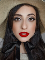 Close up headshot portrait of young natural looking casual beautiful brunette woman with trendy makeup and vibrant red lips in straw hat liten by natural light domestic room background