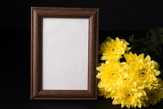 Wooden frame for a photo on a black background next to a yellow chrysanthemum. Copy space