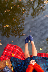 Legs of a young girl near the lake on a plaid in a red cage. Beautiful reflection in the water. View from above.