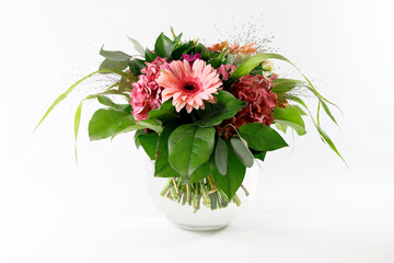 Ein feiner Festtagsstrauß mit Gerberas, Hydrangeas und Rosen in einer Kugelvase aus Glas