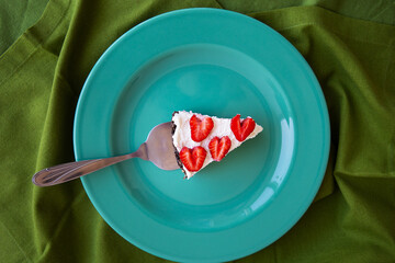 A piece of strawberry cheesecake decorated with heart-shaped strawberries lies on a mint-colored plate and stands on a green napkin. View from above.