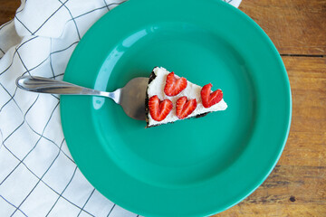 A piece of strawberry cheesecake decorated with heart-shaped strawberries lies on a mint-colored plate and stands on a checkered napkin. View from above.