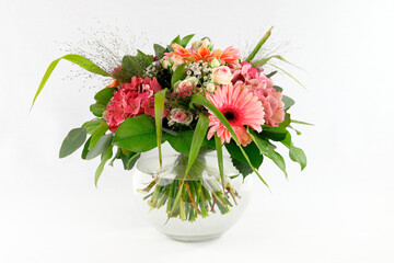 Ein feiner Festtagsstrauß mit Gerberas, Hydrangeas und Rosen in einer Kugelvase aus Glas