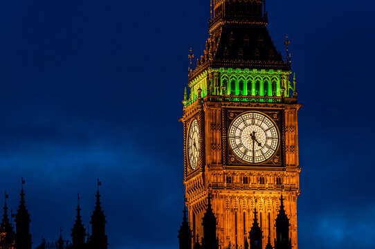 Big Ben clock face at night with silhouette of Houses of Parliament in the foreground.