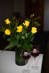 A very beautiful bouquet of yellow roses stands in a green vase and two glasses of red wine. Romantic evening.
