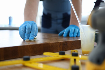 A carpenter in a workshop polishes a wooden surface. Man in gloves varnishes a board