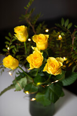 A very beautiful bouquet of yellow roses stands in a green vase, garland, lights. A romantic surprise. Close-up.