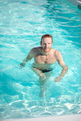 Young happy man walking in water in pool