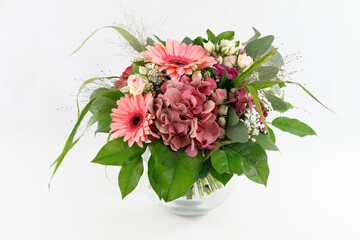 Ein feiner Festtagsstrauß mit Gerberas, Hydrangeas und Rosen in einer Kugelvase aus Glas