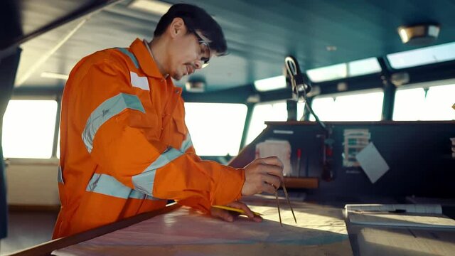 Filipino deck Officer on bridge of vessel or ship wearing coverall during navigaton watch at sea . He is plotting position on chart