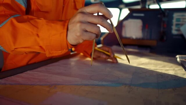 Filipino deck Officer on bridge of vessel or ship wearing coverall during navigaton watch at sea . He is plotting position on chart