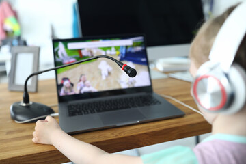 A small child sits at a table and looks at a laptop screen. Girl watching video in headphones