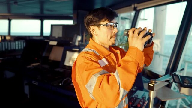 Filipino deck Officer on bridge of vessel or ship wearing coverall. He is looking through binoculars. COLREG navigaton watch at sea
